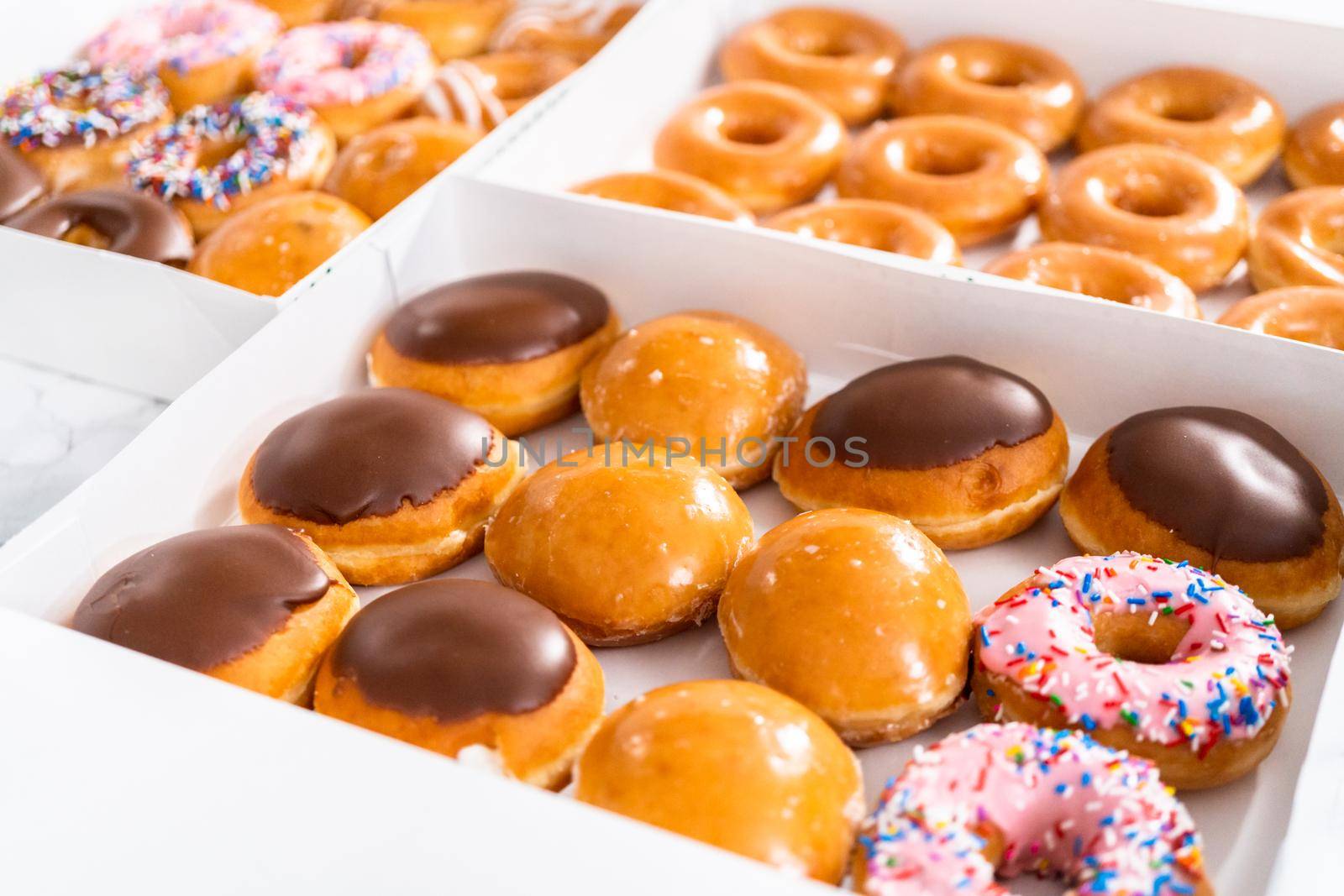 Variety of store-bought doughnuts in a white paper box.