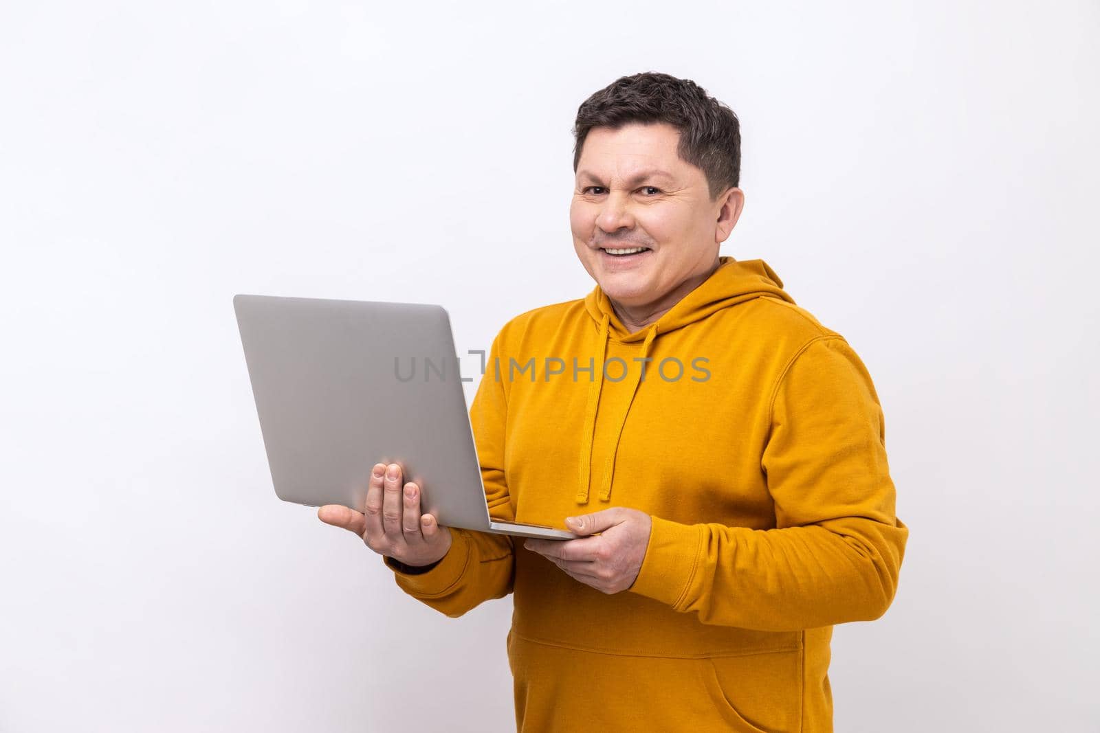 Portrait of man working on laptop typing email or chatting in social network, looking at camera with happy face expression, wearing urban style hoodie. Indoor studio shot isolated on white background.