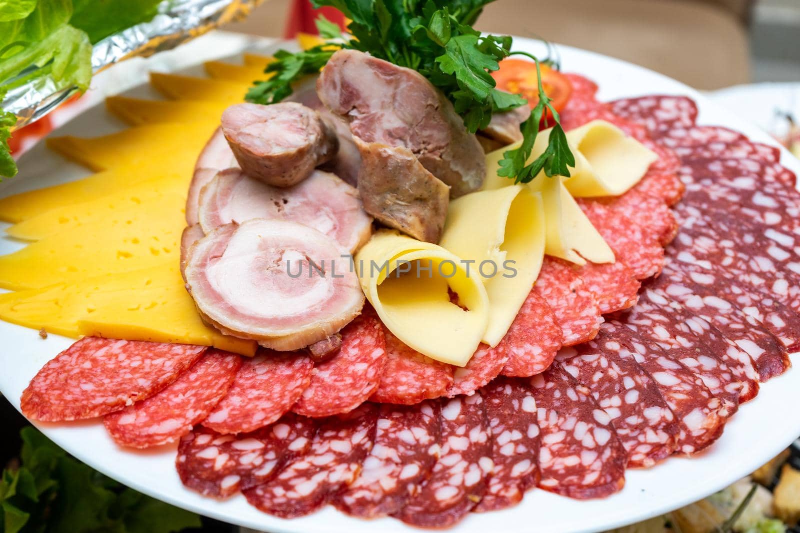 A plate of cold appetizers with various sausages, meat, and cheese. Greens and tomatoes