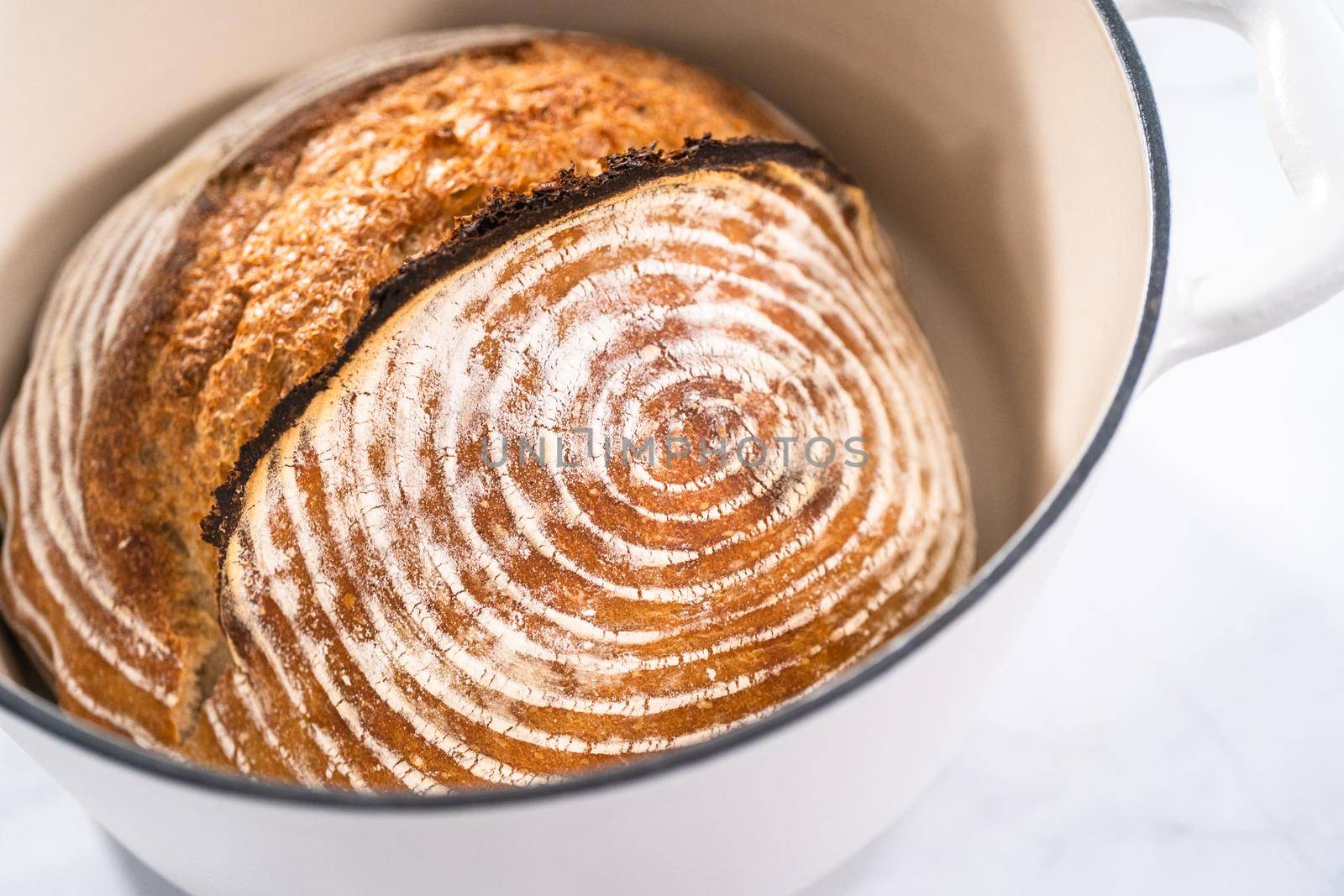 Freshly baked loaf of a wheat sourdough bread with marks from bread proofing basket in enameled cast iron dutch oven.