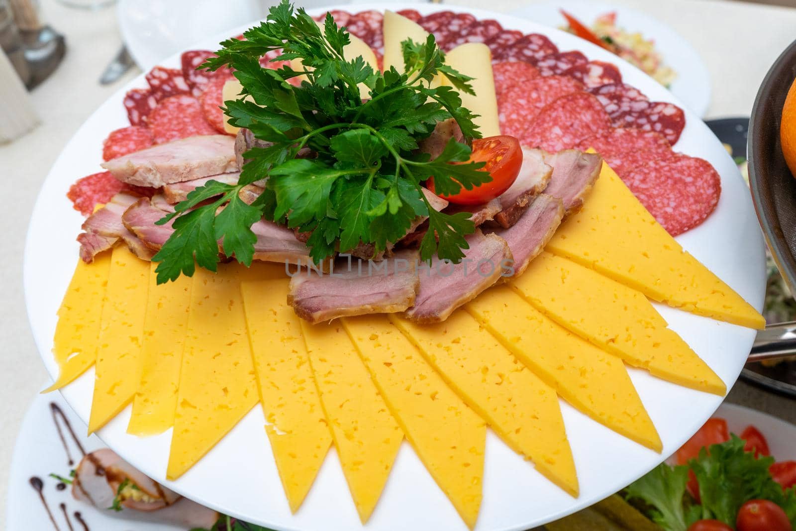 A plate of cold appetizers with various sausages, meat, and cheese. Greens and tomatoes