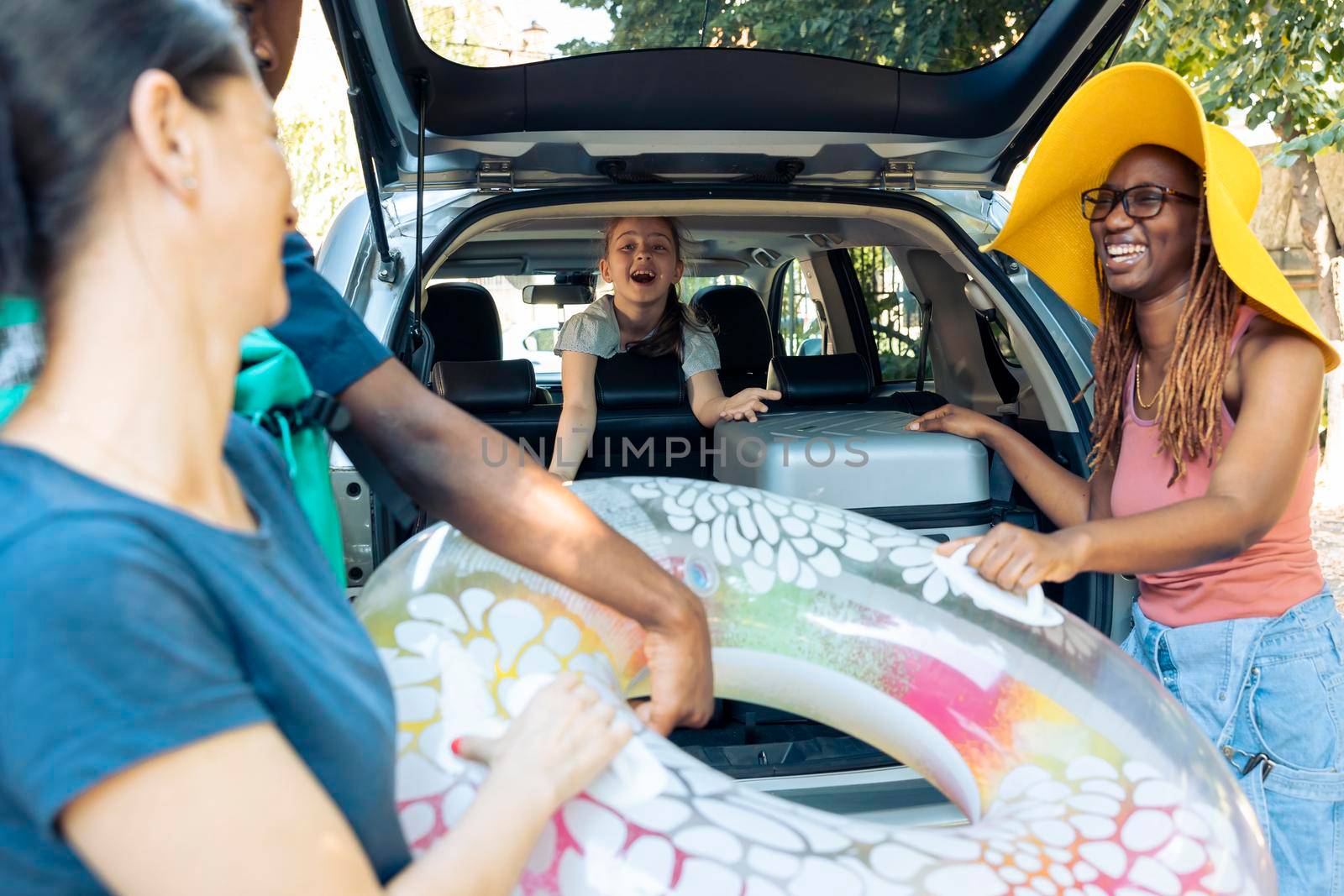 Multiethnic family and friends loading bags in car by DCStudio