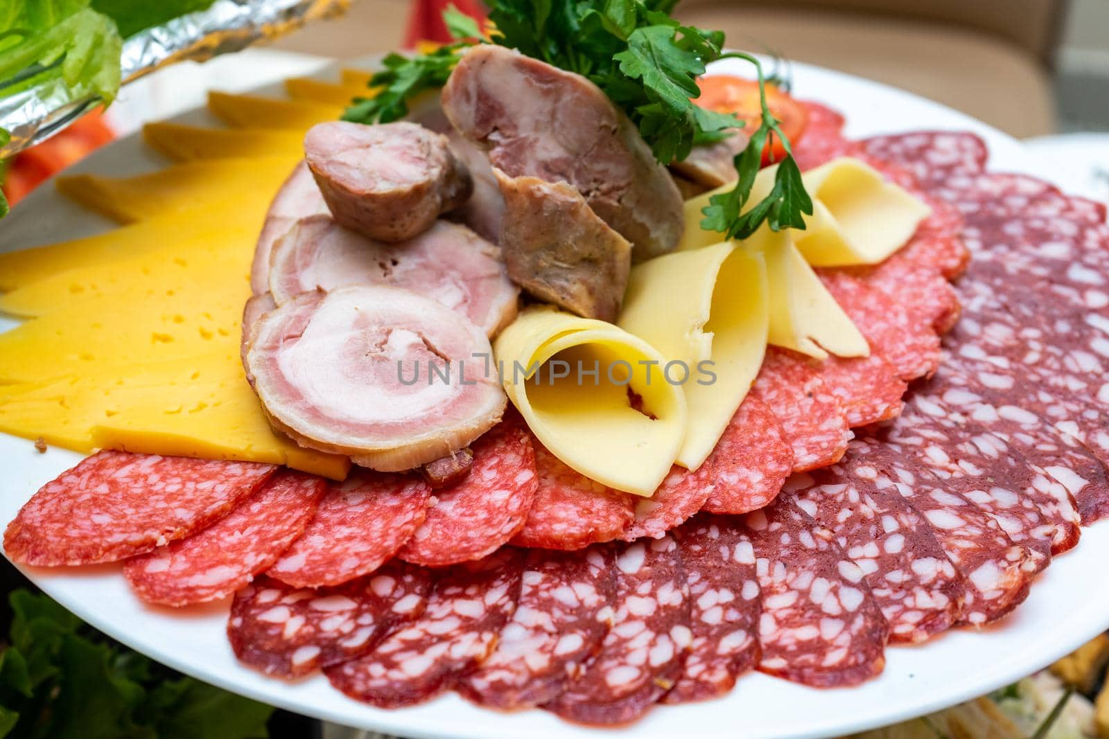 A plate of cold appetizers with various sausages, meat, and cheese. Greens and tomatoes