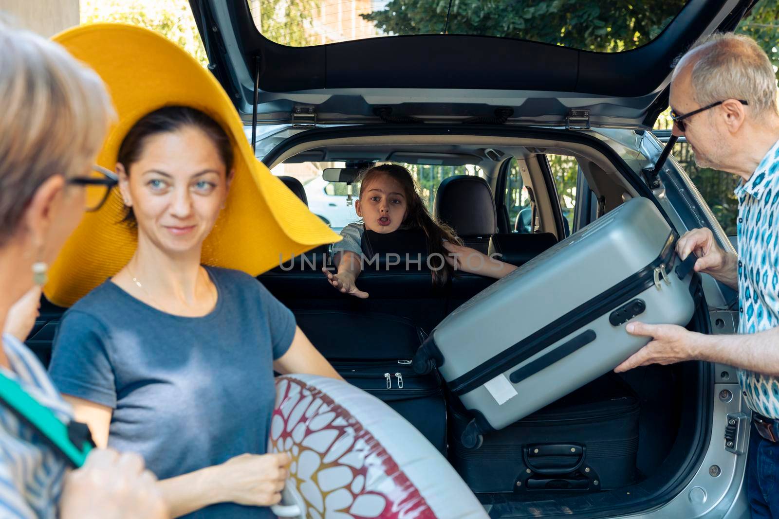 Young child going on vacation with family, preparing to leave on summer holiday at seaside with parents and grandparents. Putting luggage in vehicle trunk to travel to journey destination.