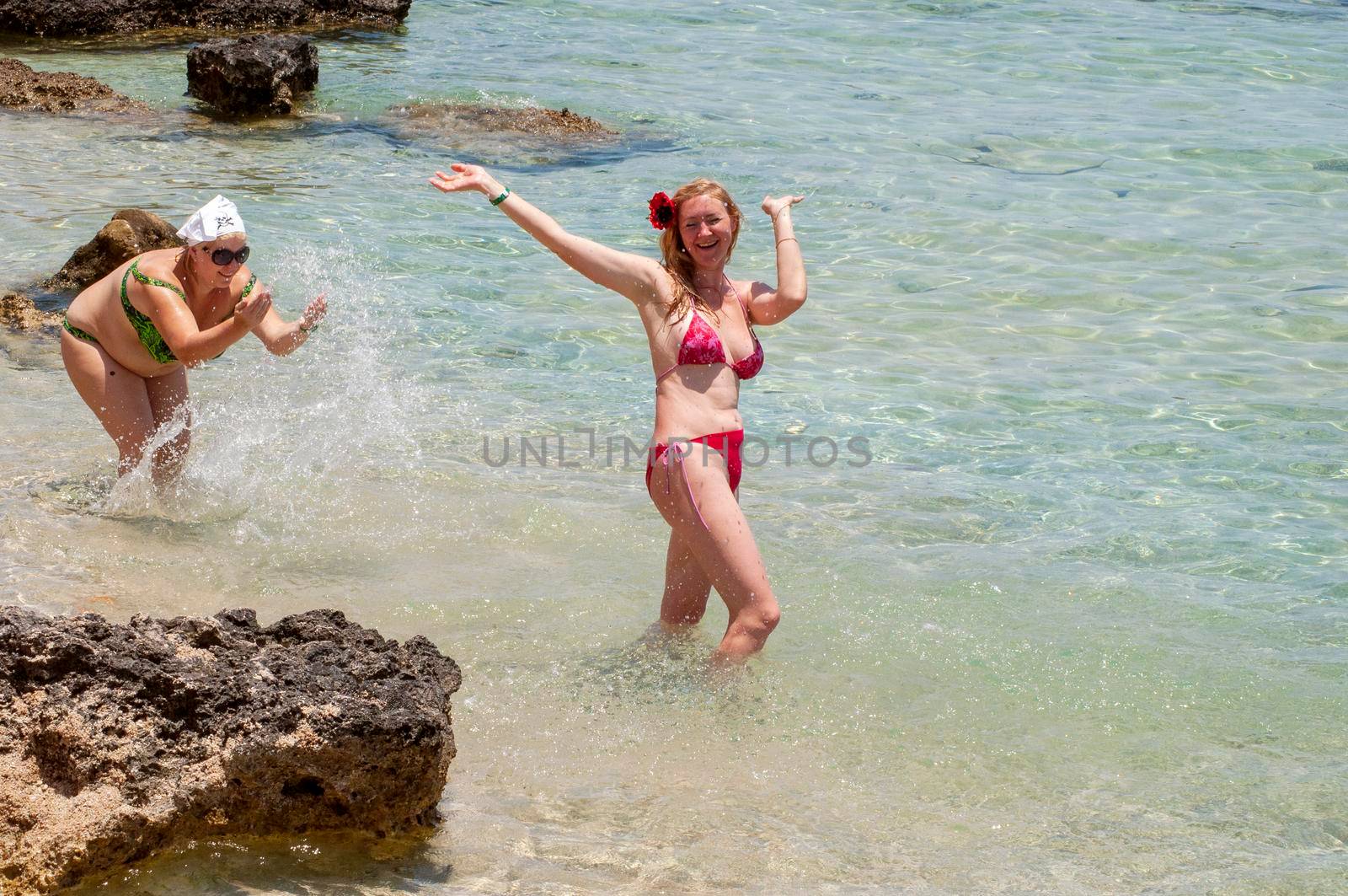two women, sisters play on the beach in the water, one splashes water on the other, freshen up in the summer on vacation by the sea. High quality photo
