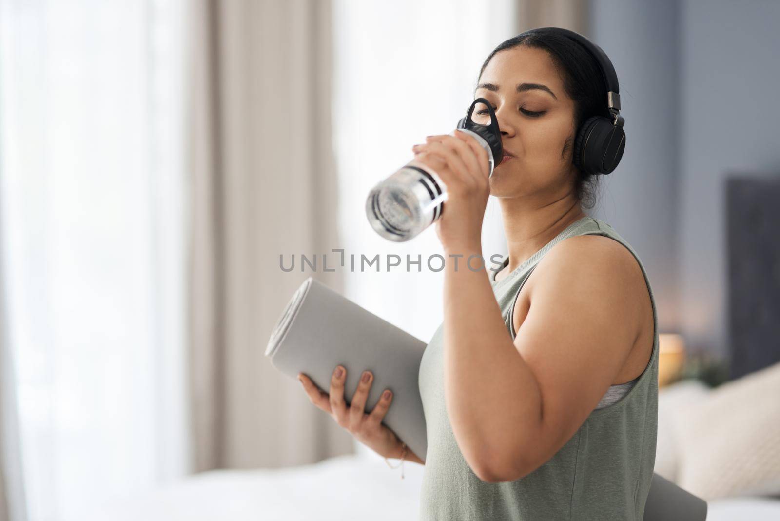 Got to stay hydrated and fuelled. a sporty young woman drinking water while exercising at home