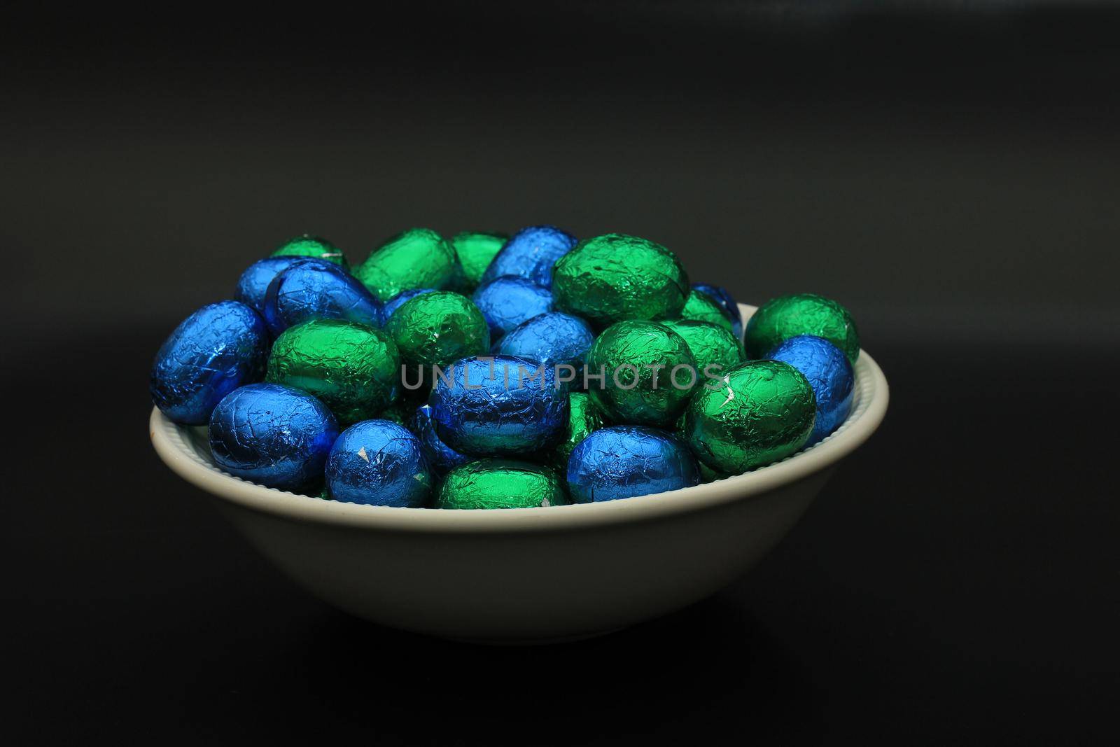 Foil wrapped chocolate easter eggs in a white porcelain bowl by studioportosabbia