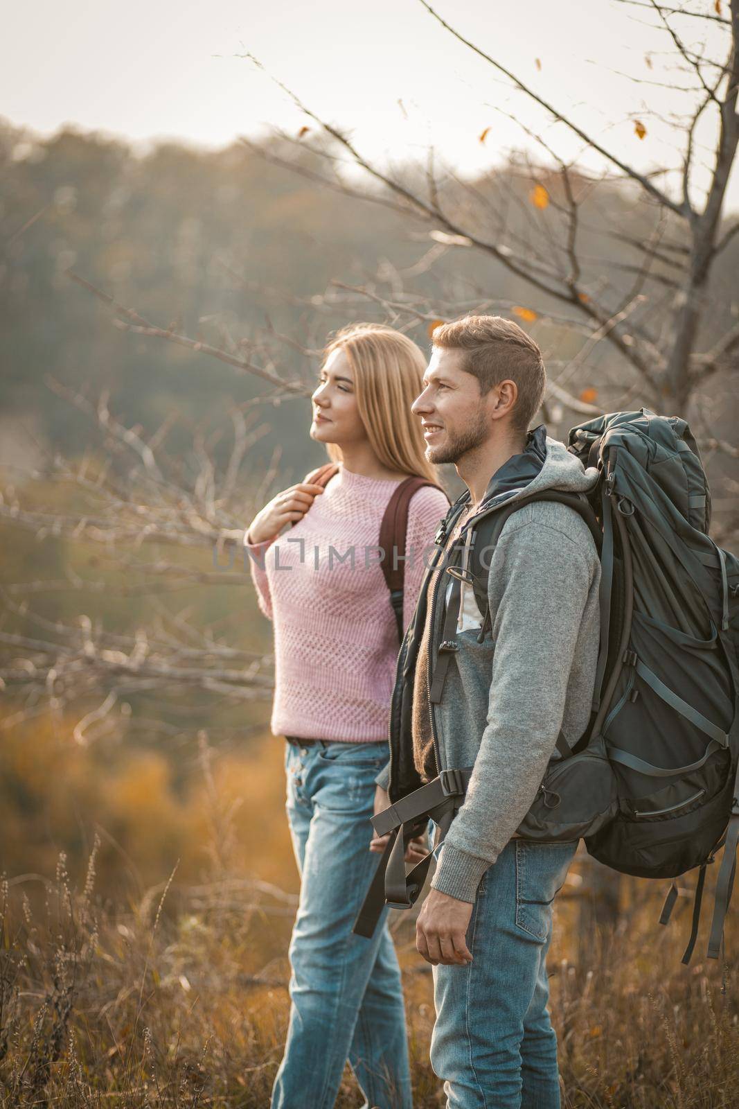 Couple of tourists admiring the natural scenery standing on a mountain side. Side view of a man and woman with backpacks are hiking in nature.