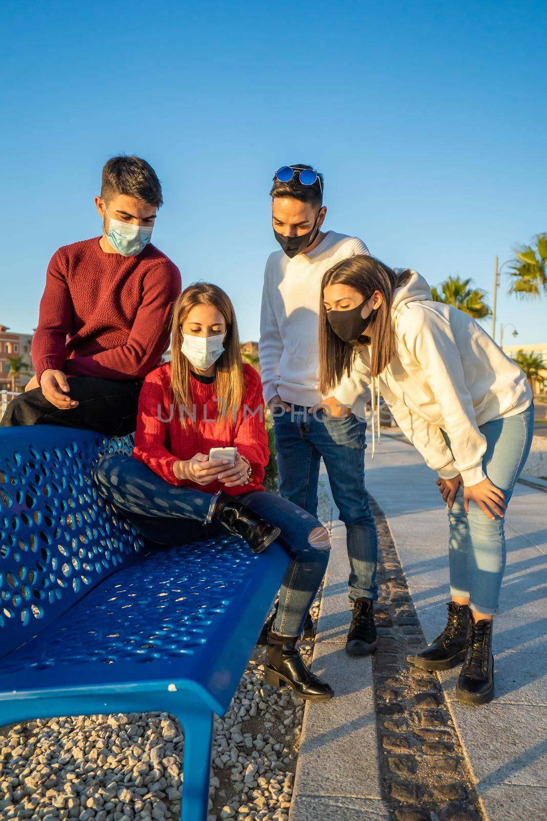 Millenial friends using smart phones wearing protective face mask on Covid wave. Worried guys and girls watching news on mobile smartphone. Travellers group stay in touch during pandemic in vacations by robbyfontanesi