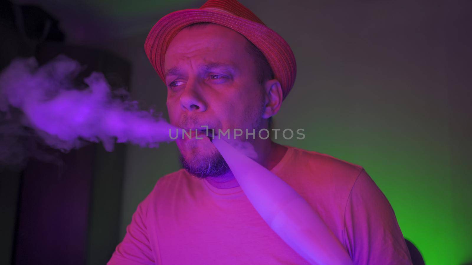 Man Exhales Smoke Smoking Of Hookah In Neon Lighting, Creative Man In Hat Smoking Hookah, Cheerful Quarantine Concept