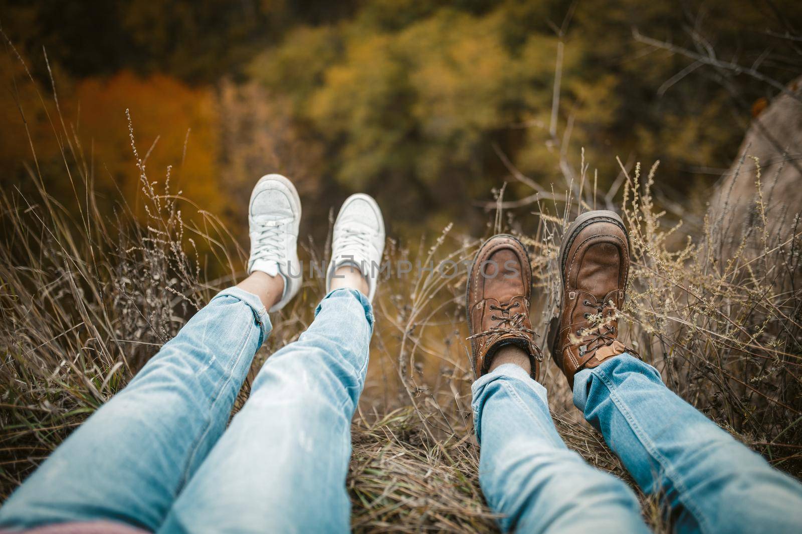 Man And Woman Rests On Cliff Edge With Legs Hanging Down by LipikStockMedia