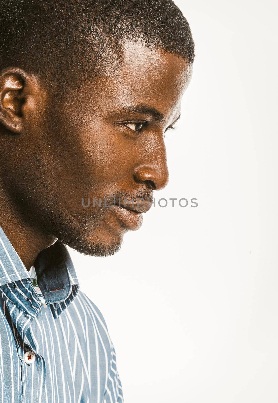 Profile view of African American man in a blue striped shirt. Close-up portrait of an attractive dark-skinned guy isolated on a white background. Copy space located at right side. Toned image.