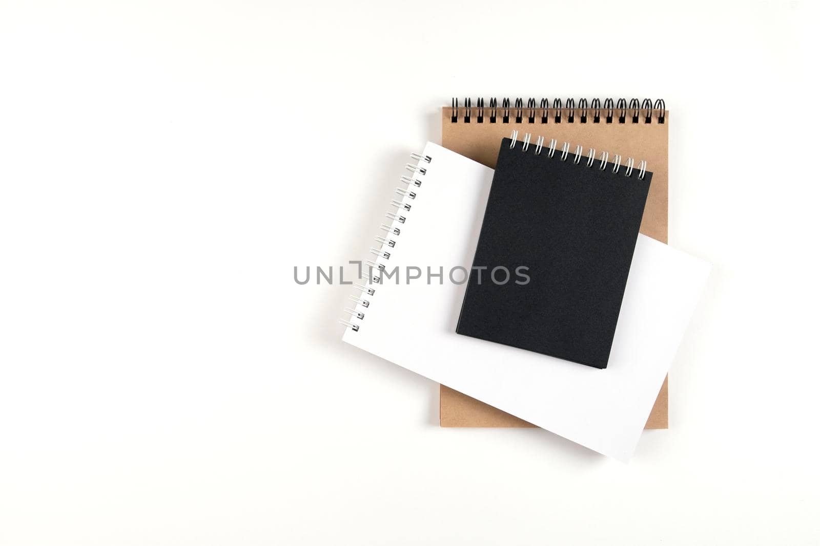 Three blank notepads on a spiral stacked in a stack on a white background. Notebooks with white, black and recycled sheets. Education, office.
