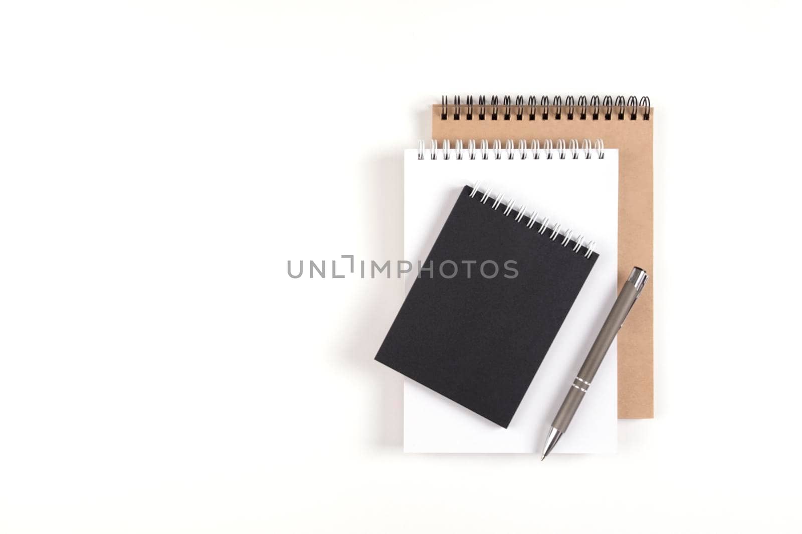 Three blank notepads on a spiral stacked in a stack on a white background. Notebooks with white, black and recycled sheets and pen. Education, office.