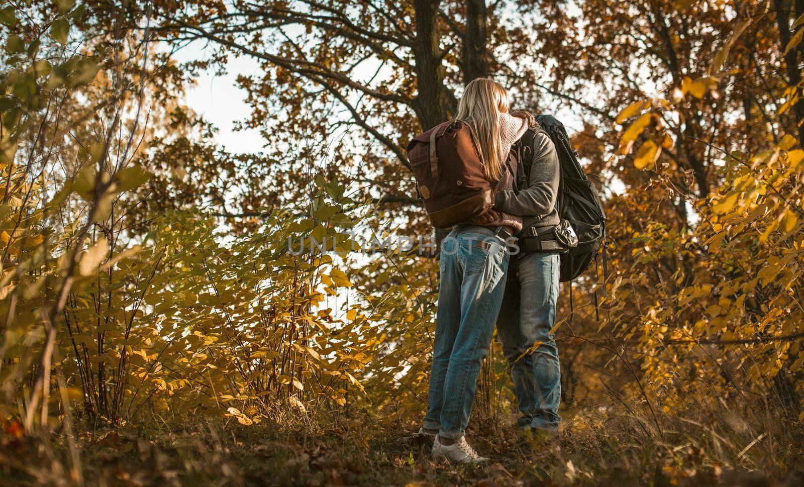 Kiss of backpackers in love hugging while standing alone against the backdrop of autumn forest outdoors. Love in nature concept.