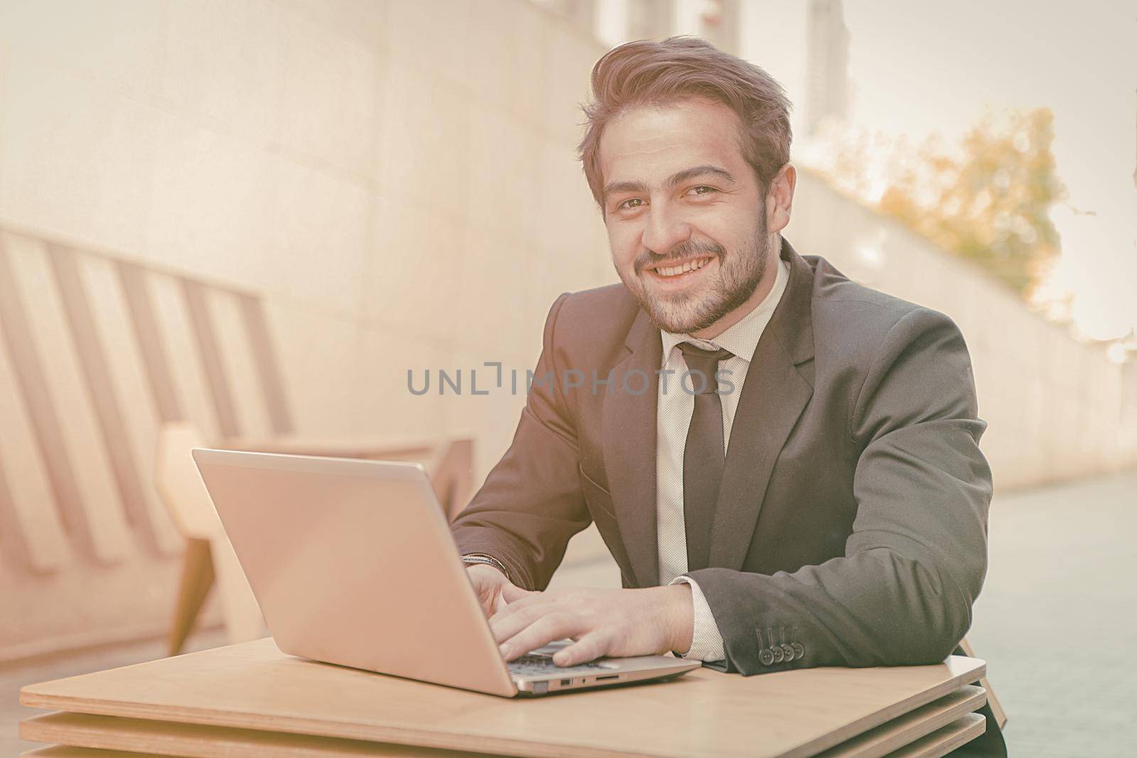 Smiling businessman laptop table for concept design. Business portrait outdoor. Wireless communication. Business without office concept. Business technology. Business career concept by LipikStockMedia