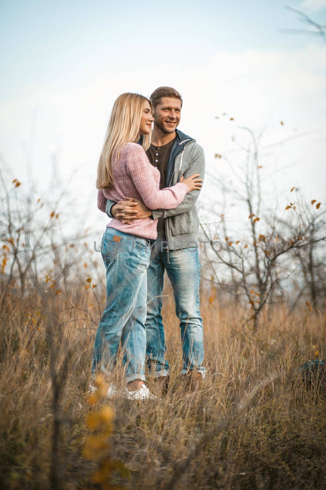 Hugging couple smiling standing on autumn grass outdoors, young guys cuddling in nature against a blue sky, full growth view.