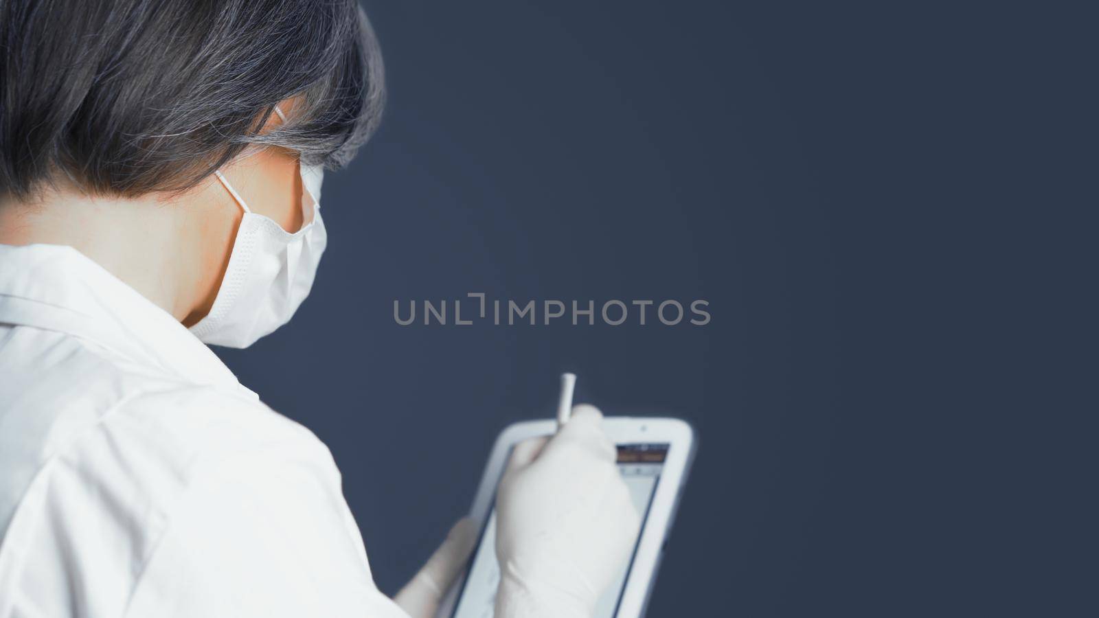 Health officer works with digital tablet. Gray-haired female doctor make notes in electronic database on digital gadget, rear or side view.