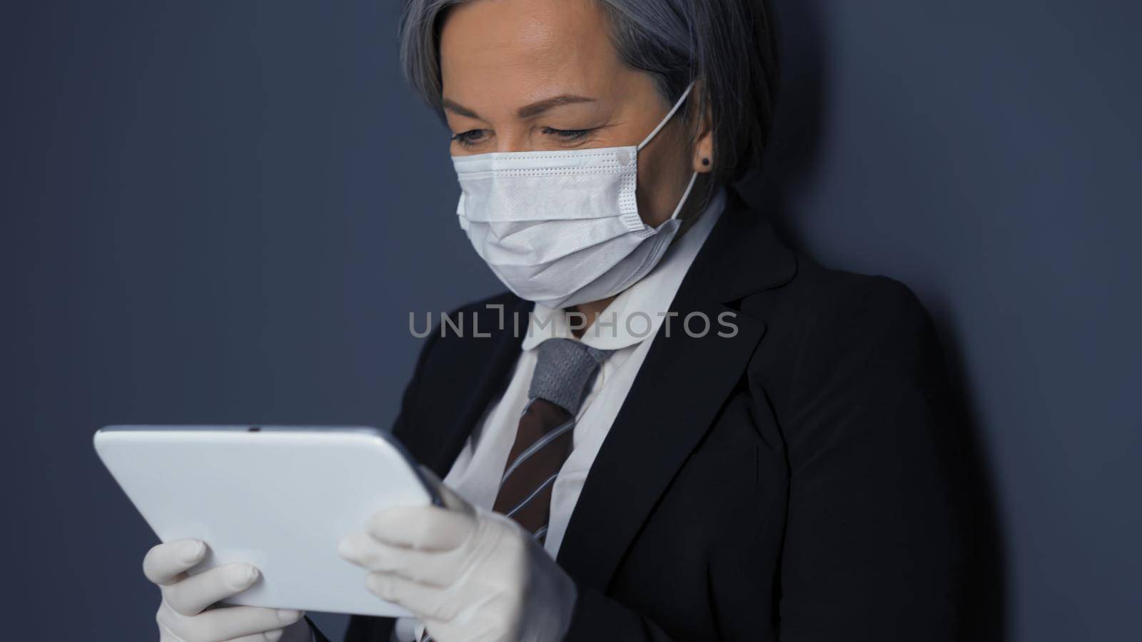Businesswoman in mask looks at screen of digital tablet. Wireless technology concept. Pandemic concept.