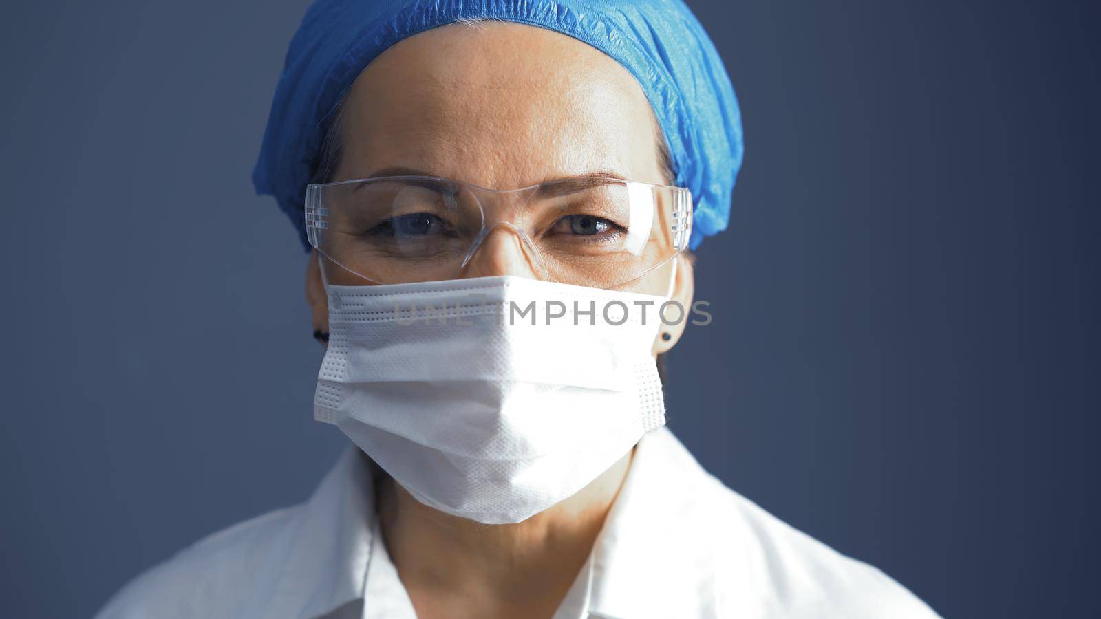 Mature female doctor in mask and goggles portrait. Caucasian woman, lab medical worker on gray back. Close up shot by LipikStockMedia