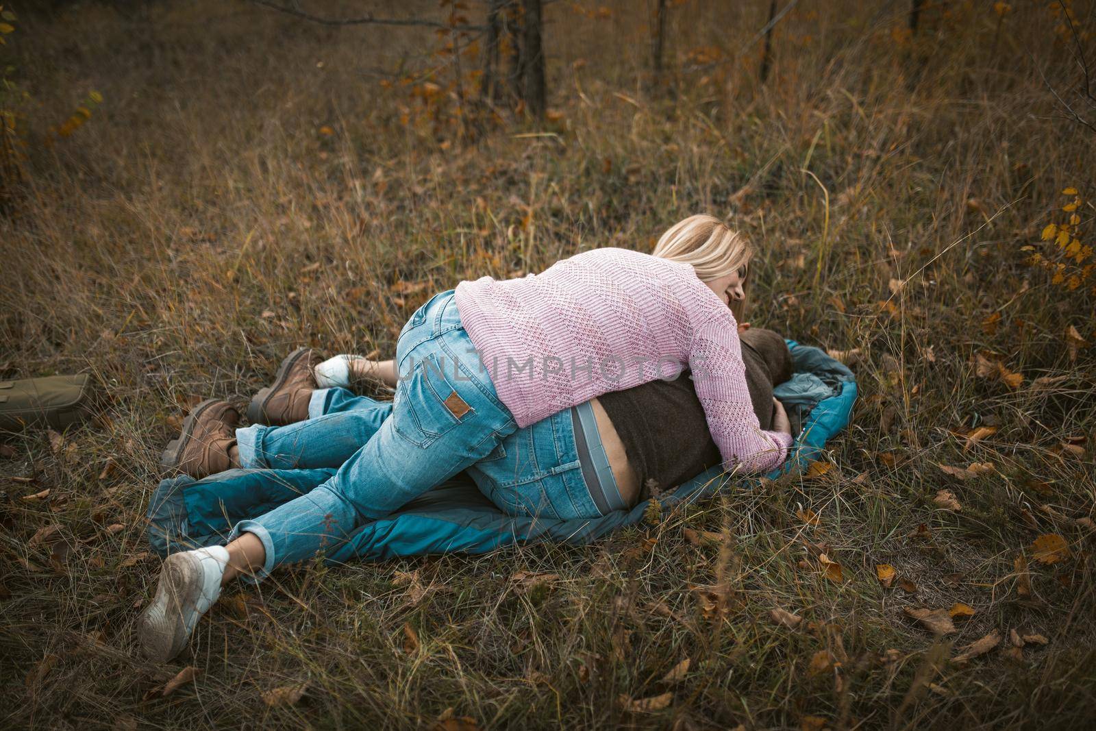 Cute Couple Fooling Around While Lying On Sleeping Bag At Grass, Blonde Woman Laughs Leaning On Her Caucasian Man In Casual Clothes, Fun In Nature Concept