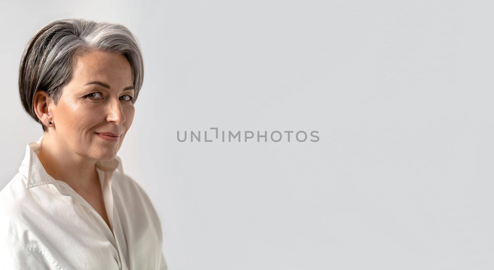 Caucasian mid adult woman smiles slightly looking at camera isolated on white background. Close up portrait. Copy spase for text. Horizontal blank for ad banner. Maturity concept by LipikStockMedia
