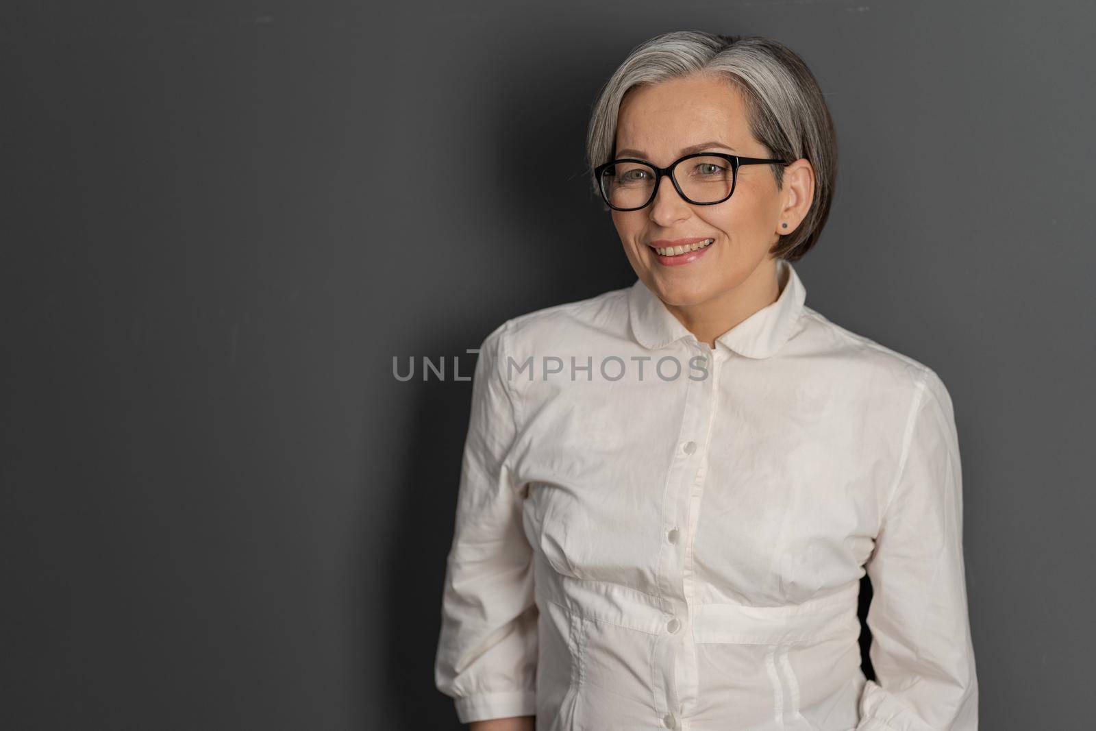 Intelligent middle aged woman with glasses smiling charmingly while looking at copy space on the left. Business concept. education or science concept by LipikStockMedia