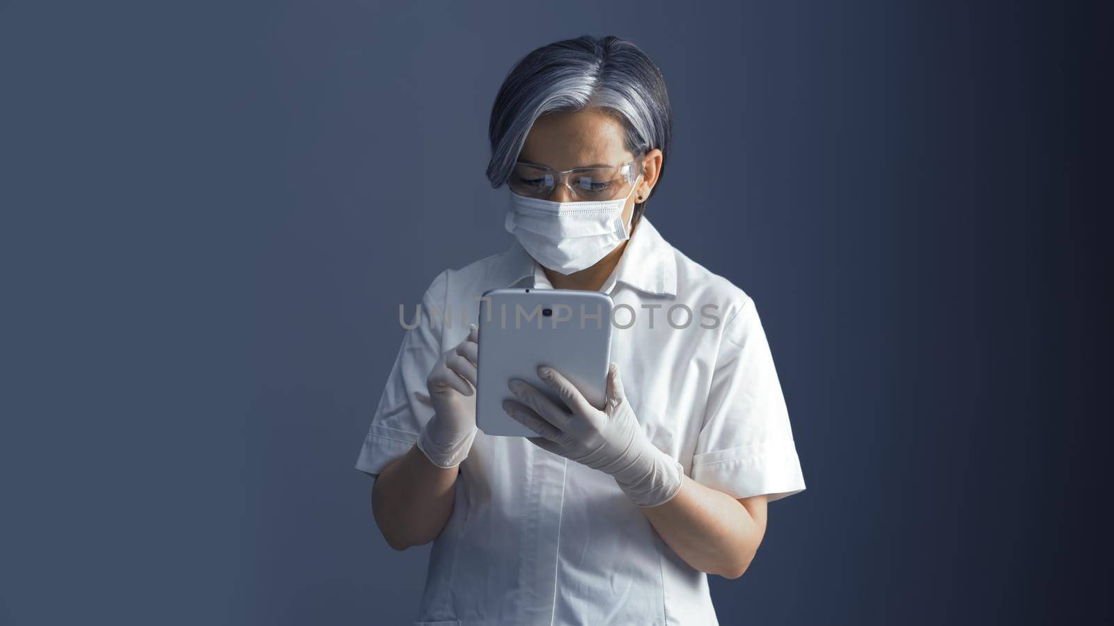 Female doctor works with database on digital tablet. Gray- haired woman in medical uniform works with electronic gadget.
