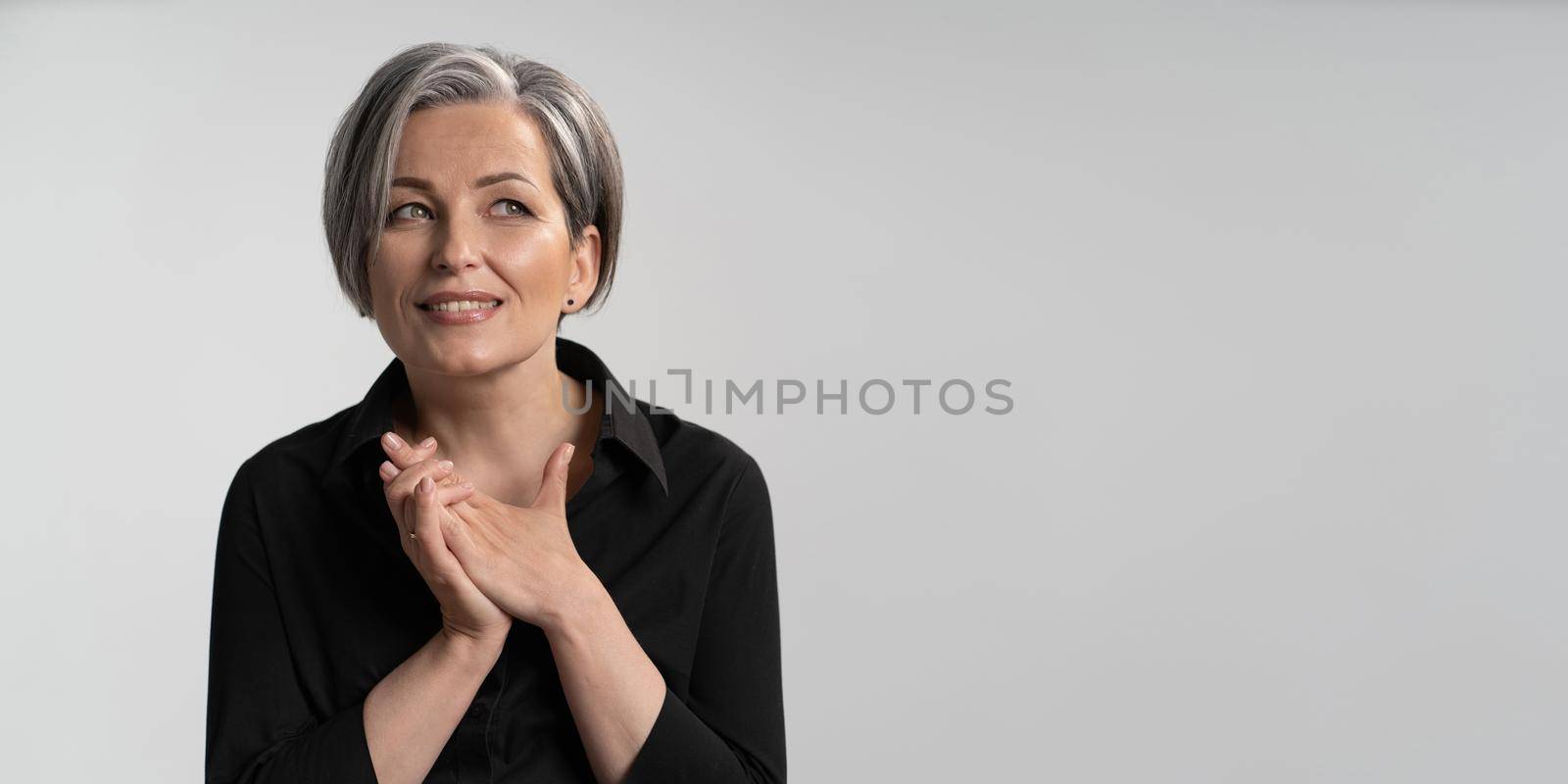 Smiling silver haired woman dreams clasped hands. Caucasian mature woman in black blouse looking to right side with copy or text spase. Cut out on white background. Horizontal blank or template.