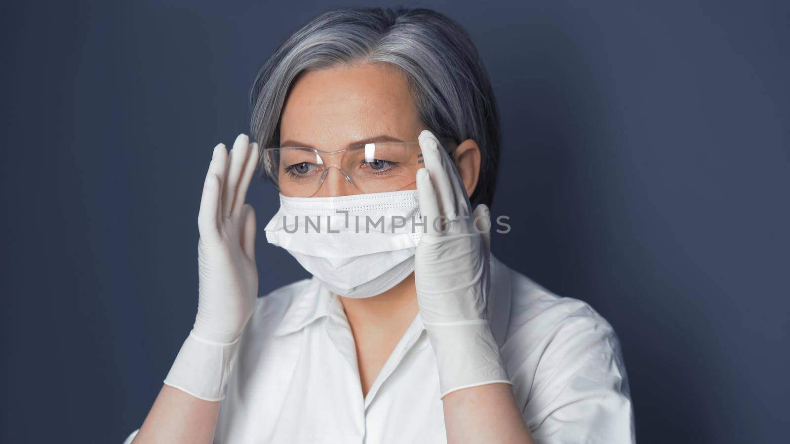 Doctor in uniform adjusts safety glasses. Cute Caucasian woman wearing protective mask and disposable gloves adjusts her glasses. Close up portrait. Toned image by LipikStockMedia