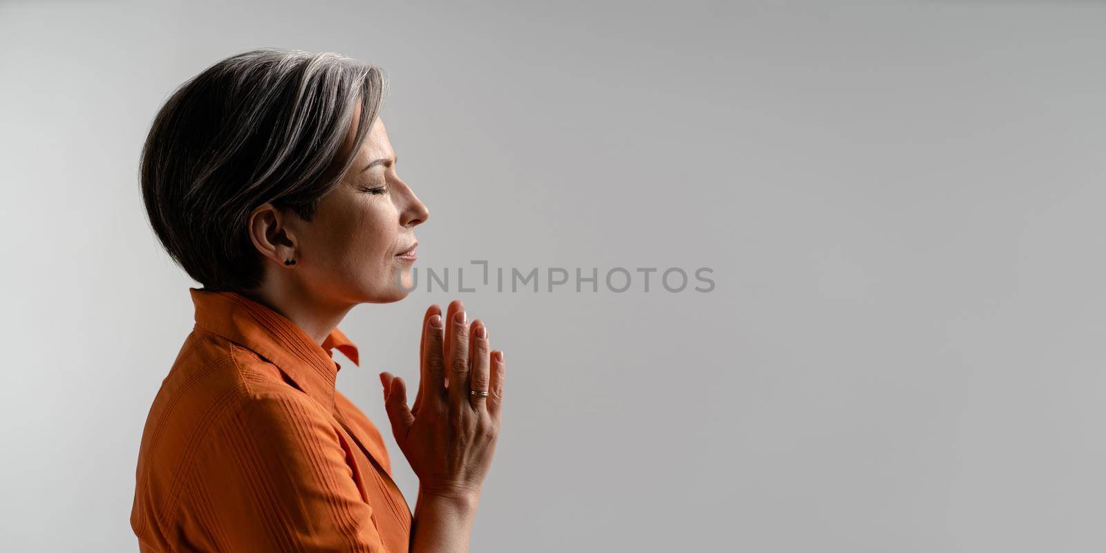 Mature woman folded hands for prayer. Spiritual Caucasian woman closed eyes. meditation concept. Profile view. Horizontal template for ad banner with copy spase for text at right.