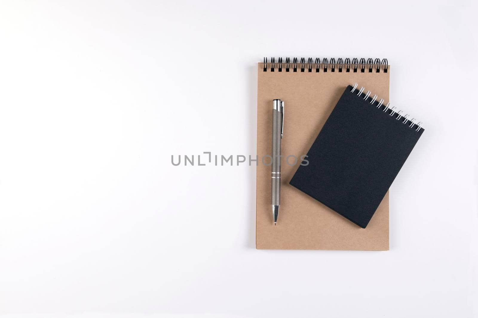 Two blank spiral notepads stacked on a white background next to an automatic pen. Notepads with black and recycled sheets. Education, office.