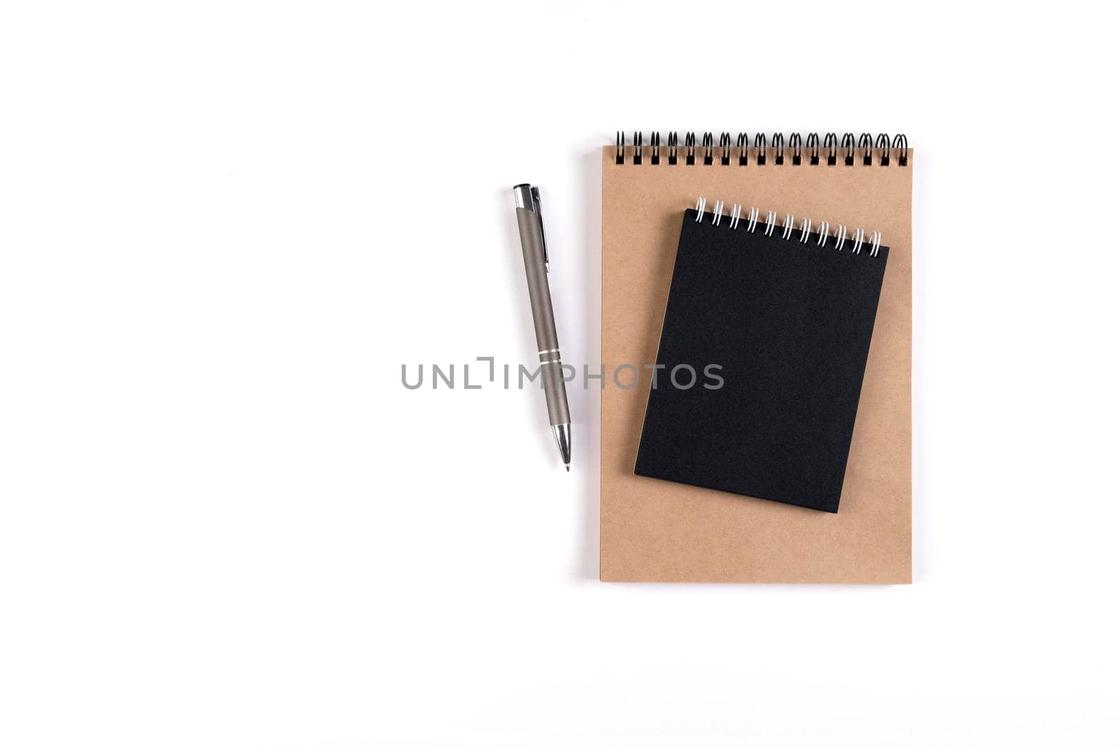 Two blank spiral notepads stacked on a white background next to an automatic pen. Notepads with black and recycled sheets. Education, office.