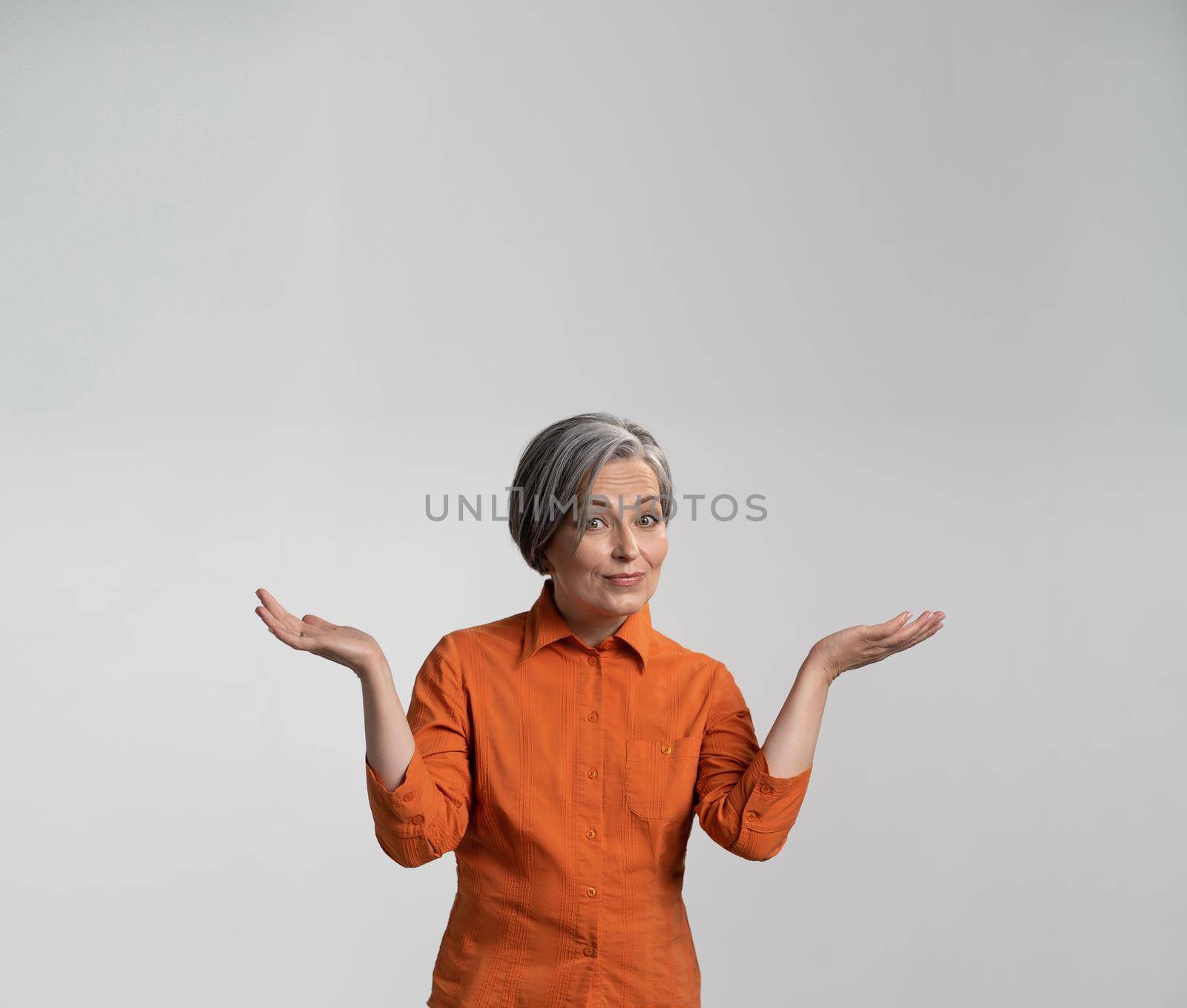 Surprised mid-aged woman presents an advertising product smiling at camera with opened palms. Copy spase for text. Square template for publication on social networks by LipikStockMedia