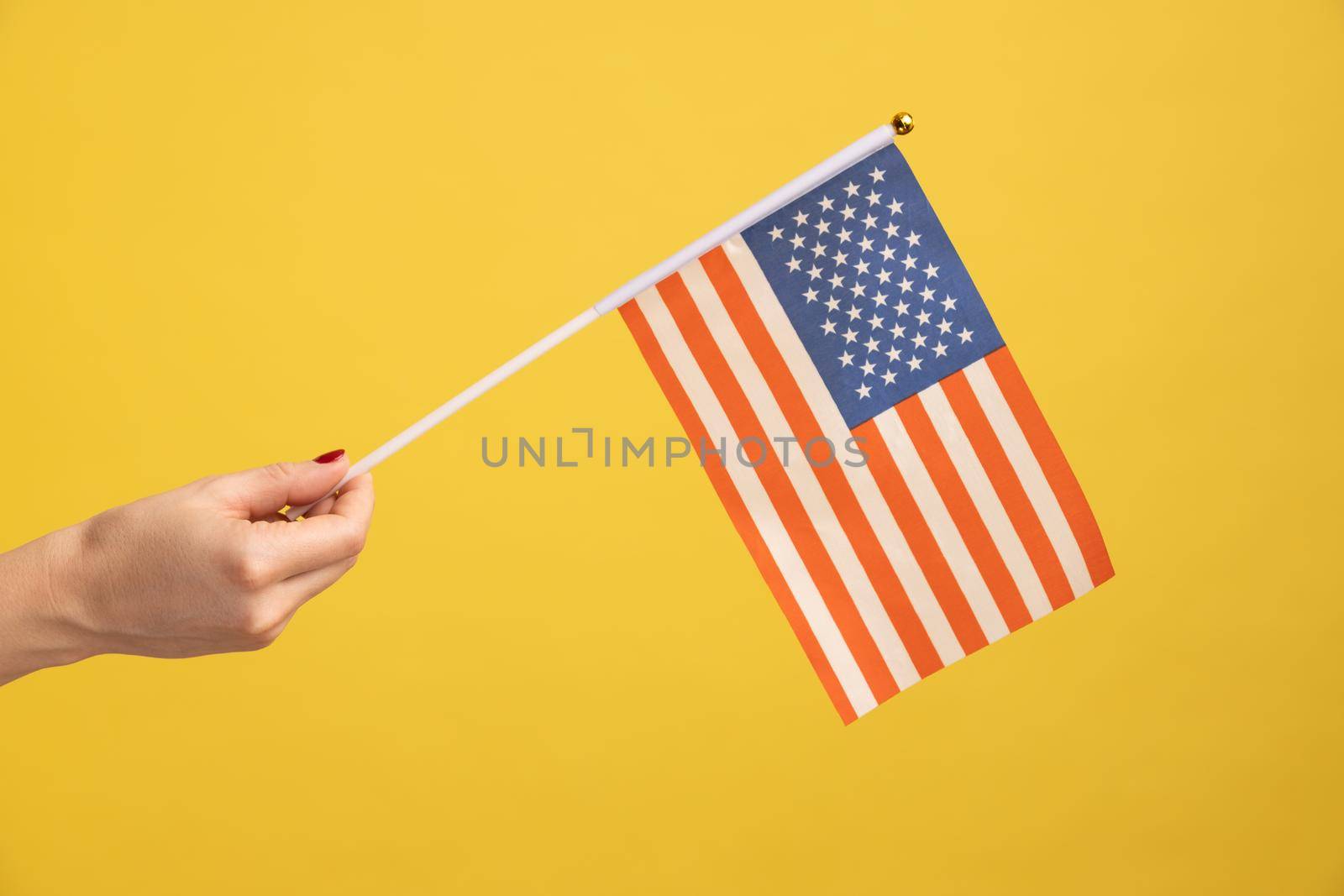 Profile side view closeup of human hand holding USA national flag. United states of America. National independance day - 4th july. Indoor studio shot isolated on yellow background.