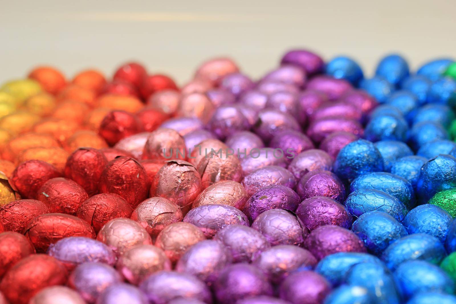 a group of foil wrapped chocolate easter eggs in rainbow colors by studioportosabbia