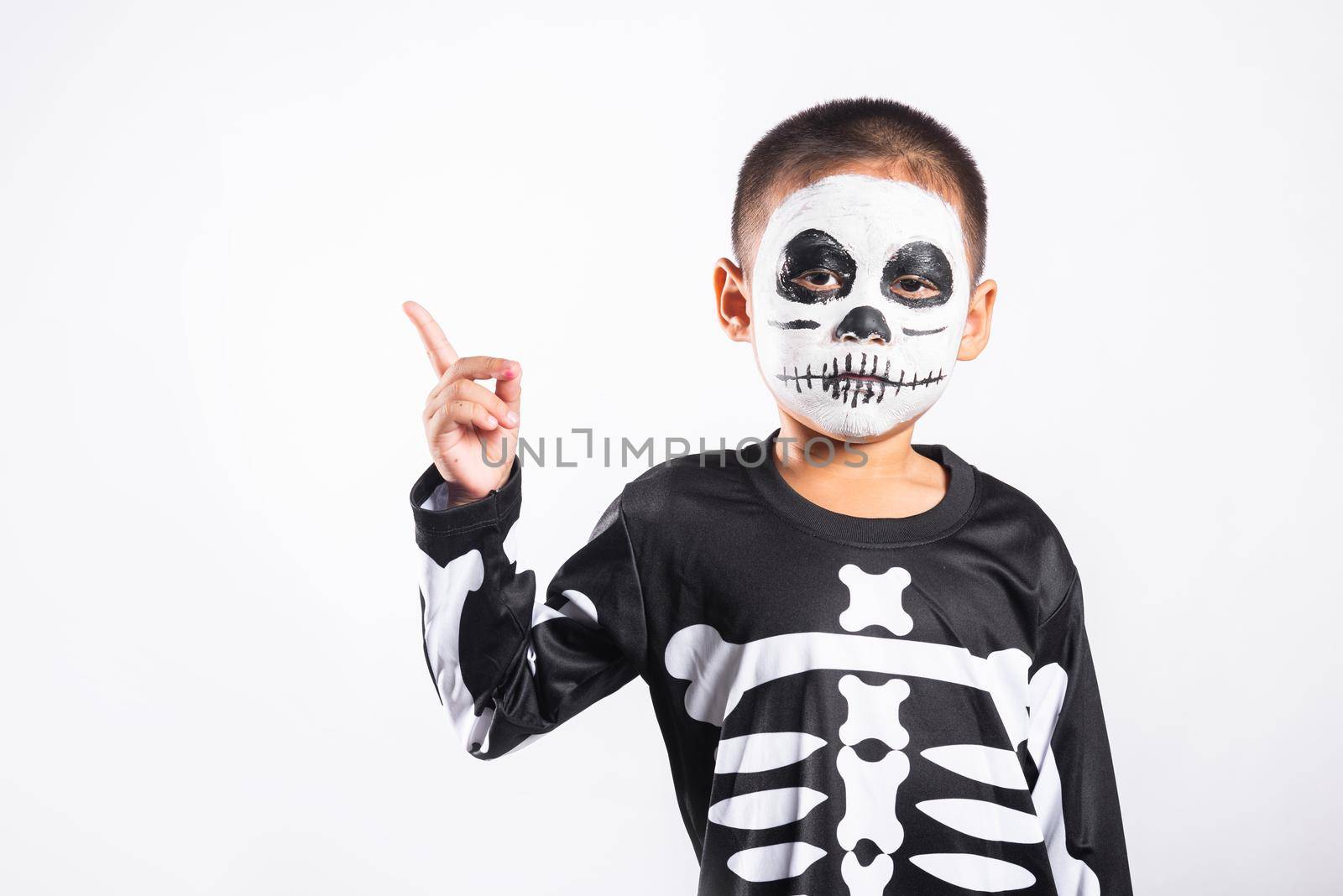 Halloween Kid. Child man horror face painting make up for ghost scary point finger to side space, Portrait of little boy wearing skeleton costume isolated white background, Happy halloween day concept