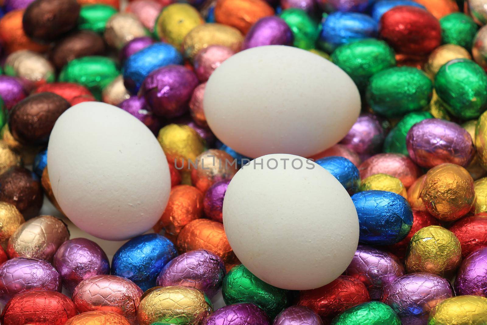 Hen eggs on a pile of colorful wrapped chocolate easter eggs