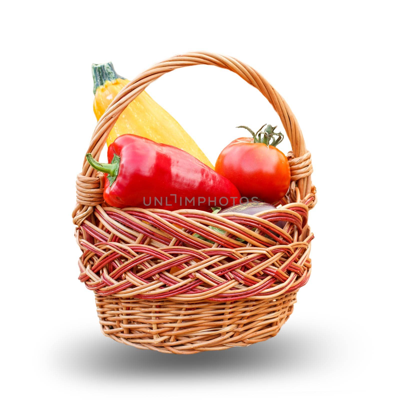 Just picked zucchini, tomato and bell pepper in a wicker basket on the white isolated background. Just harvested vegetables.