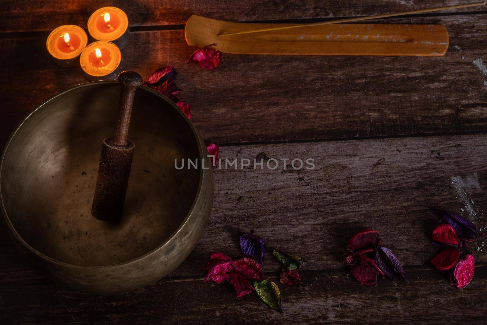 handmade tibetan bowl with flower petals and candles in dim light