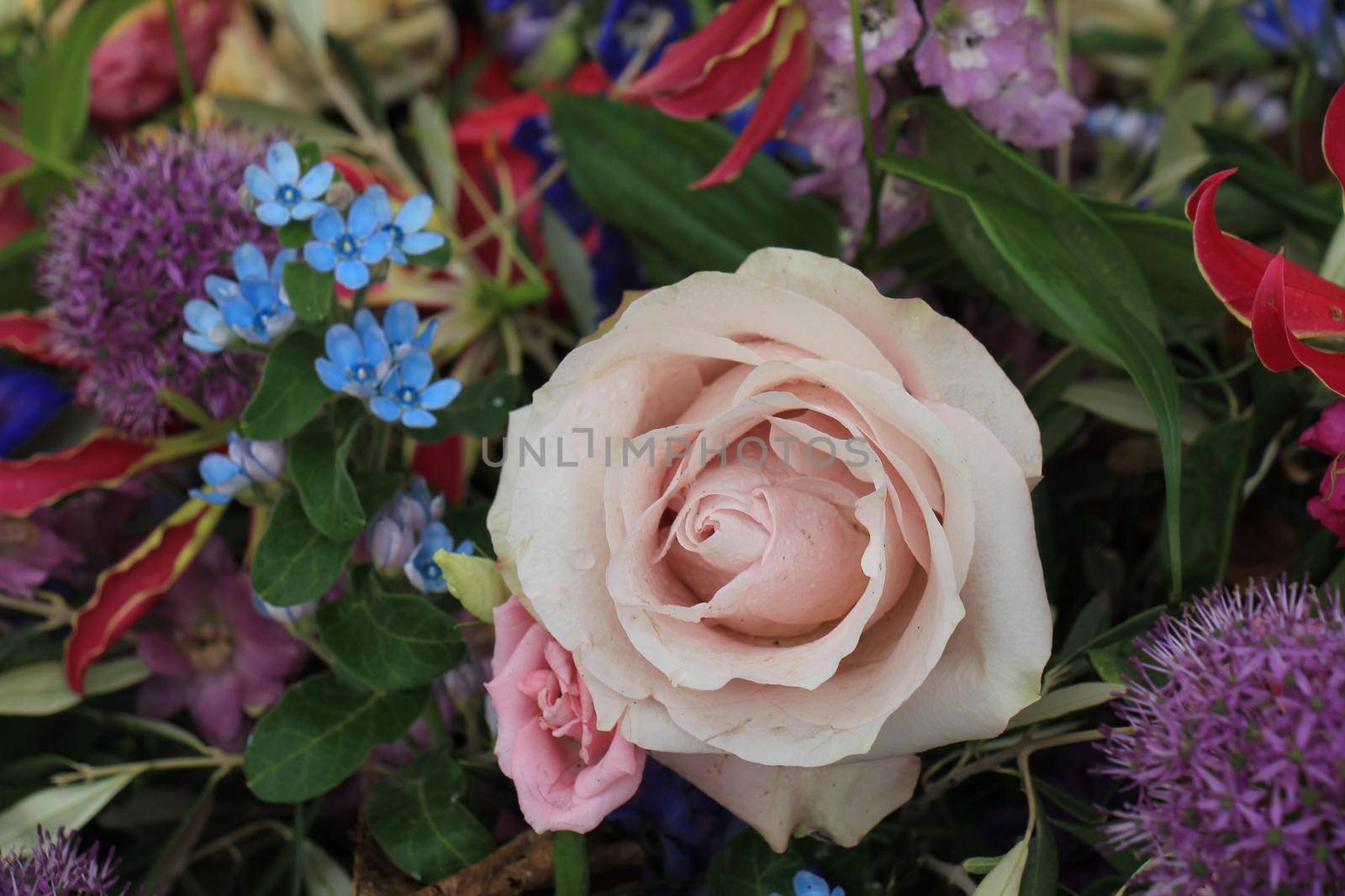 Big purple rose in a floral wedding decoration with small blue and purple flowers