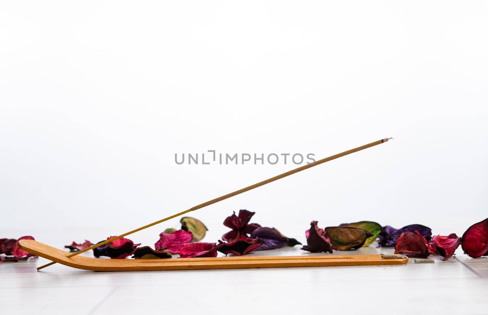 lighted incense stick in its holder with flower petals on a white background and copy-space