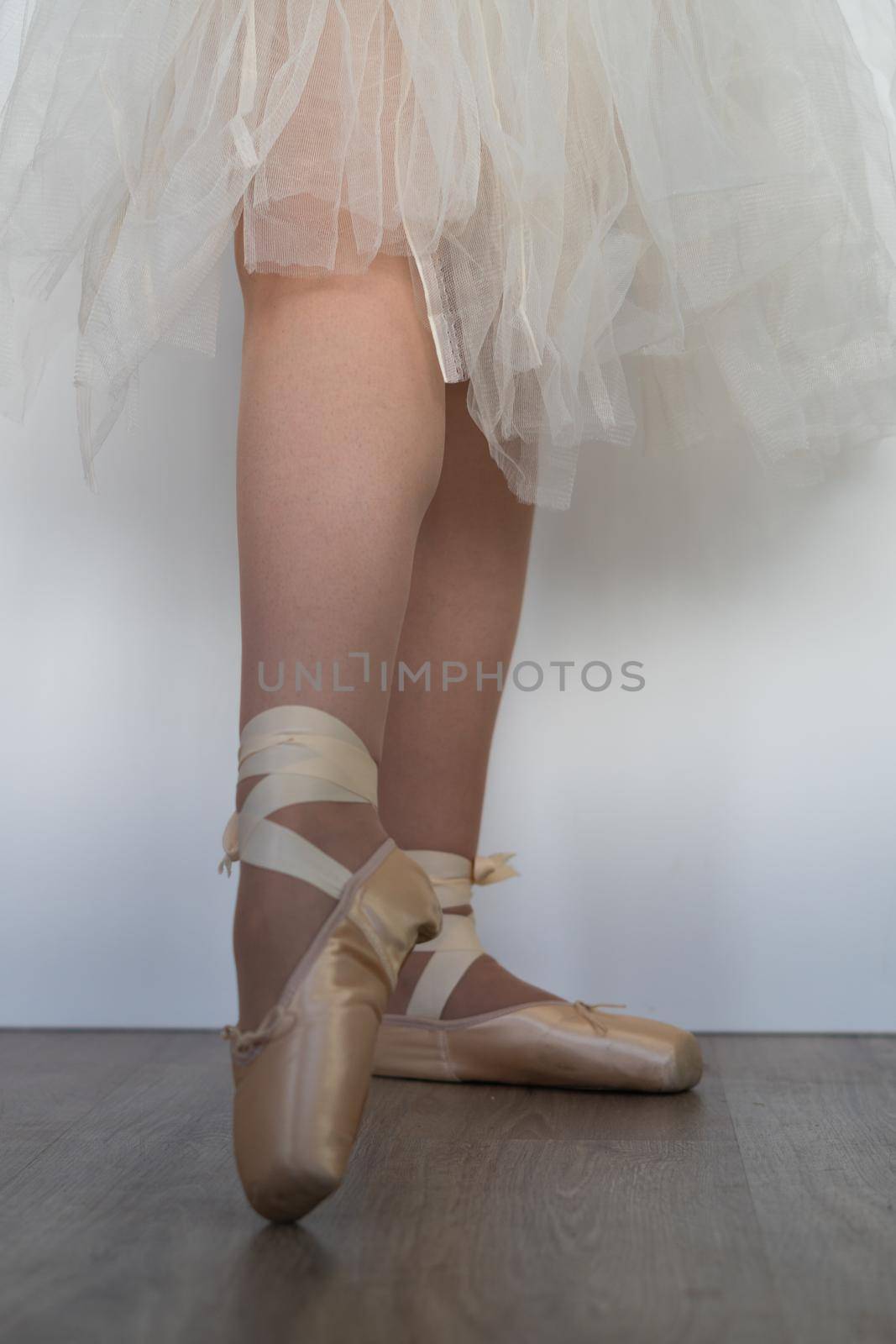 legs of girl dancing ballet with tulle skirt and pink shoes different dance steps wooden floor and white background with copy space