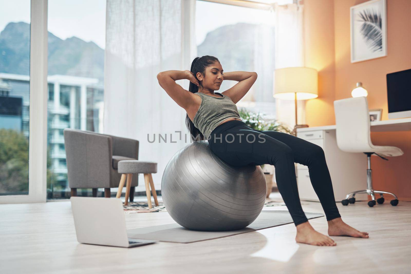 Getting fitter with virtual sessions. a woman working out in her living room with her laptop next to her. by YuriArcurs