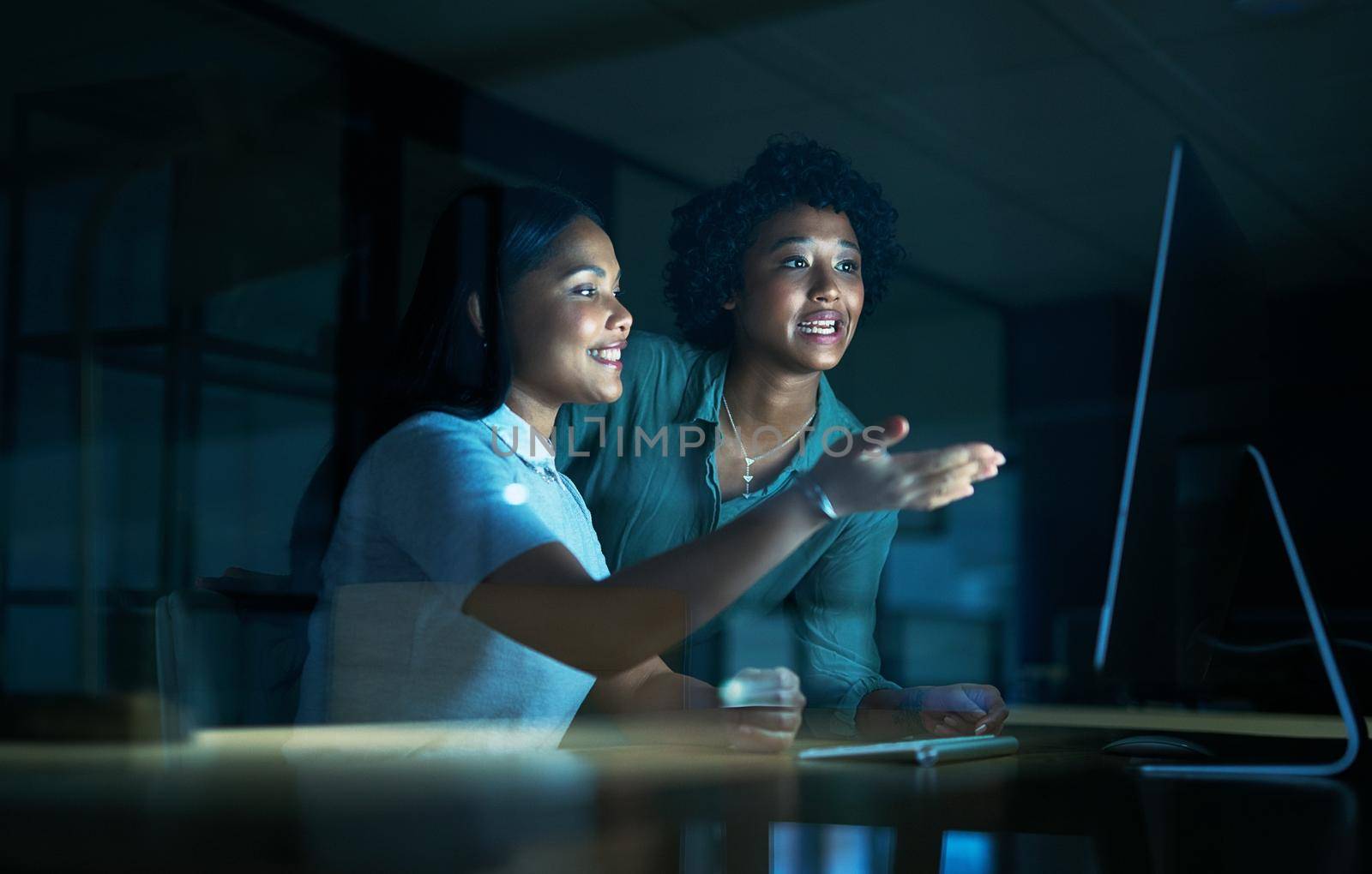 Good communication gets good results. two young businesswomen using a computer together during a late night at work. by YuriArcurs