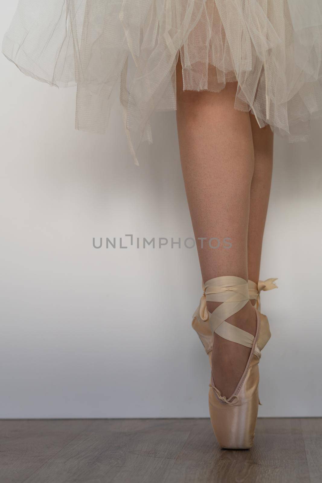 legs of girl dancing ballet with tulle skirt and pink shoes different dance steps wooden floor and white background with copy space