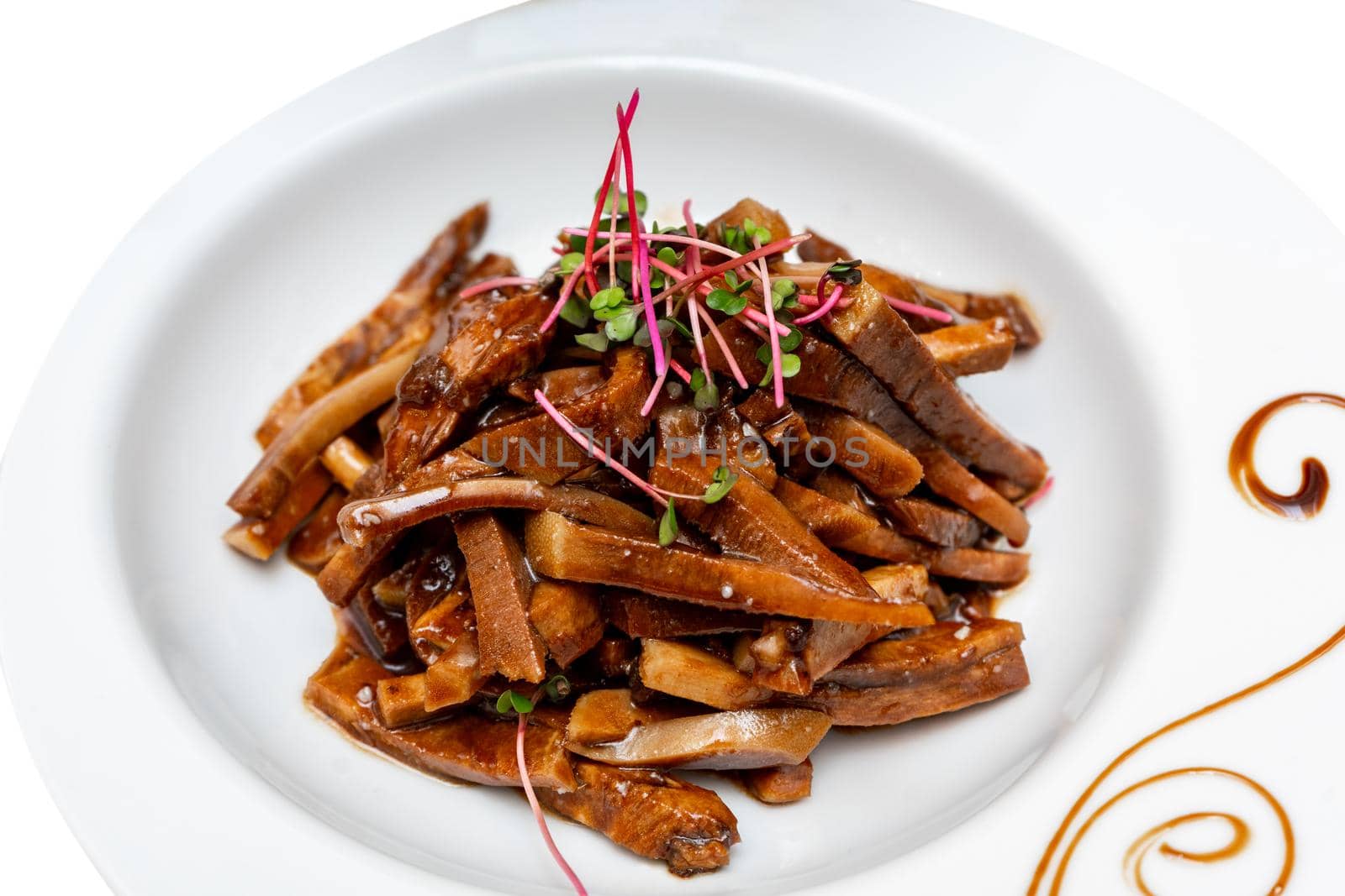 Fried pieces of pork in sauce decorated with microgreens. Marinated pig ears.