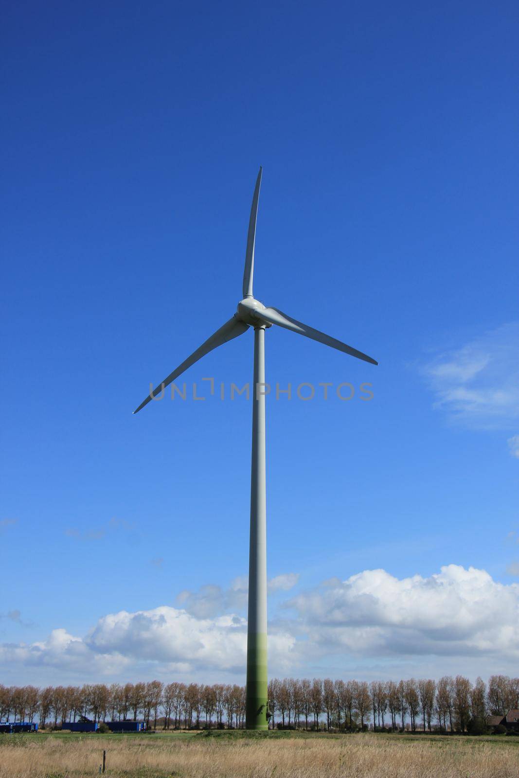 A Wind turbine generating electricity in a blue sky by studioportosabbia