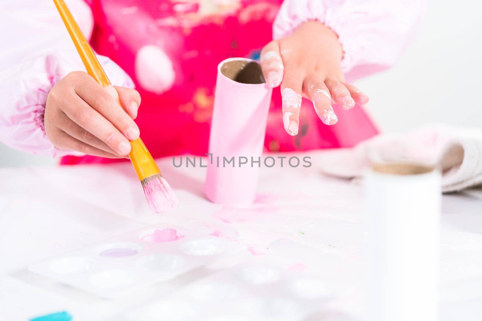 Little girl making a unicorn out of the toilet paper roll and craft paper.