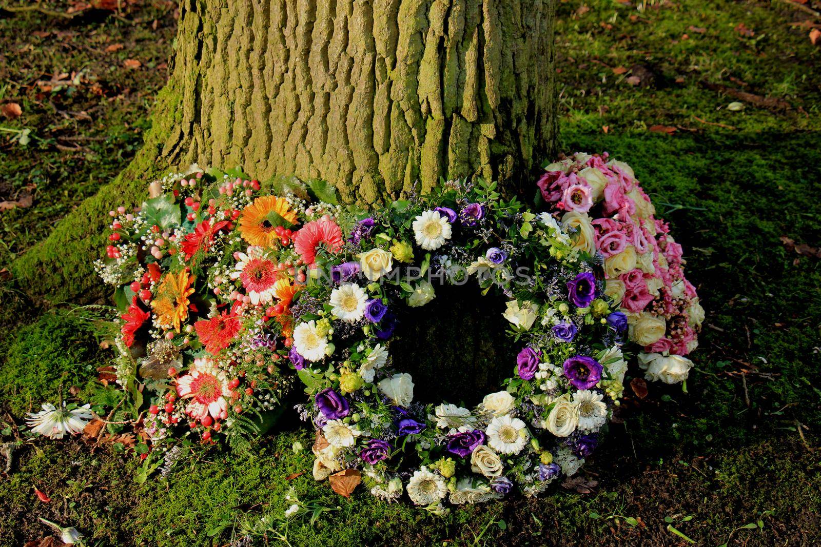 Sympathy wreath or funeral flowers near a tree by studioportosabbia